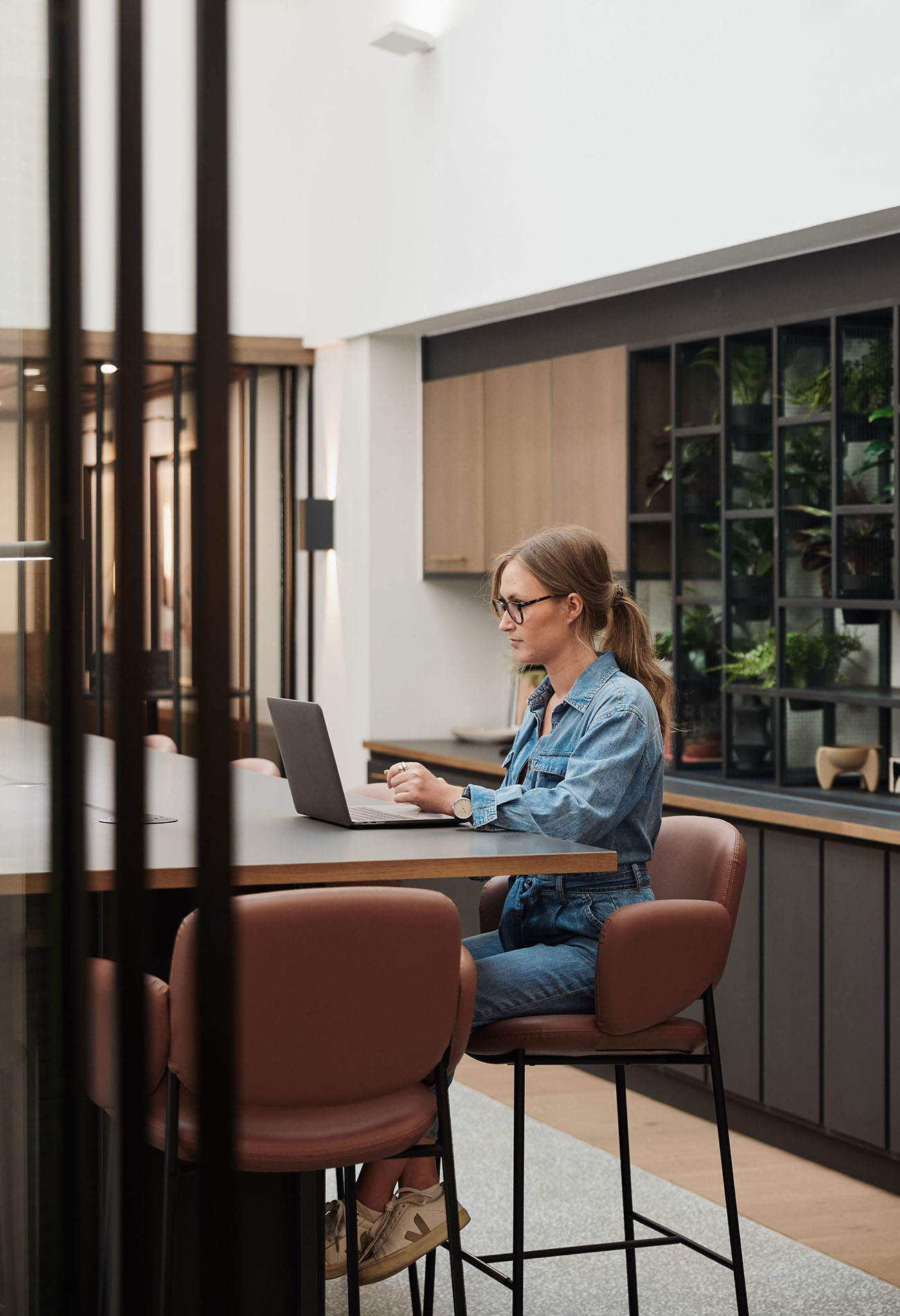 Lady using laptop on high stool at large table